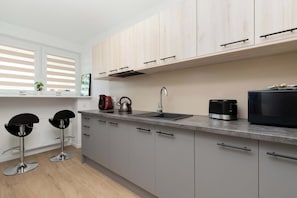 Uma cozinha moderna com armários de madeira clara, uma pia de aço inoxidável e um micro-ondas.