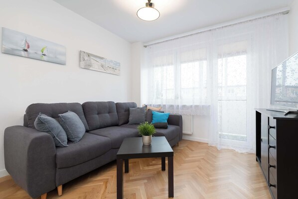 A modern living room with a grey sofa, a small black table with a plant, and a black cabinet.