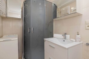 A bathroom with a modern design, including a large mirror, a sink with toiletries, and a shower enclosure.