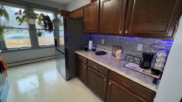 Una cocina con armarios de madera, un refrigerador, una encimera con cafetera y una ventana con plantas.