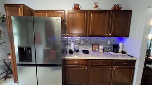 Una cocina con gabinetes de madera, un refrigerador de acero inoxidable, un salpicadero de azulejos y varios utensilios de cocina sobre la encimera.