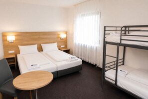 A hotel room with a double bed, a bunk bed, a small round table, and a chair. - Hotel Allee 25 (Stuttgart)