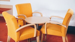 A room with a round table and four yellow chairs, a white sofa, and a wooden floor. - Hotel Allee 25 (Stuttgart)