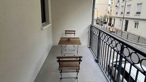 A balcony with a wooden table and two benches, a window, and a view of buildings and parked cars. - Elegant Appt - 1bdr/2p - Near Paris & La Defense (Suresnes)