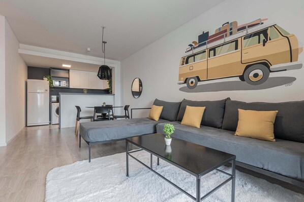 A modern living room with a gray sofa, a coffee table, and a kitchen area in the background.