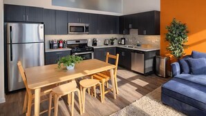 Une cuisine moderne avec des meubles de couleur sombre, des appareils électroménagers en acier inoxydable et une table à manger en bois.
