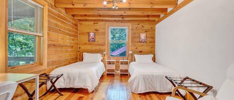 Una cabaña con dos camas, pisos de madera, un ventilador de techo y una ventana con persianas.