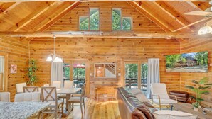 A log cabin interior with a dining area, seating, and a view of the outdoors. - Eagles Rest~ Grand, Luxurious & Peaceful— Near Hiking Trails & Virginia Tech! (New Castle)