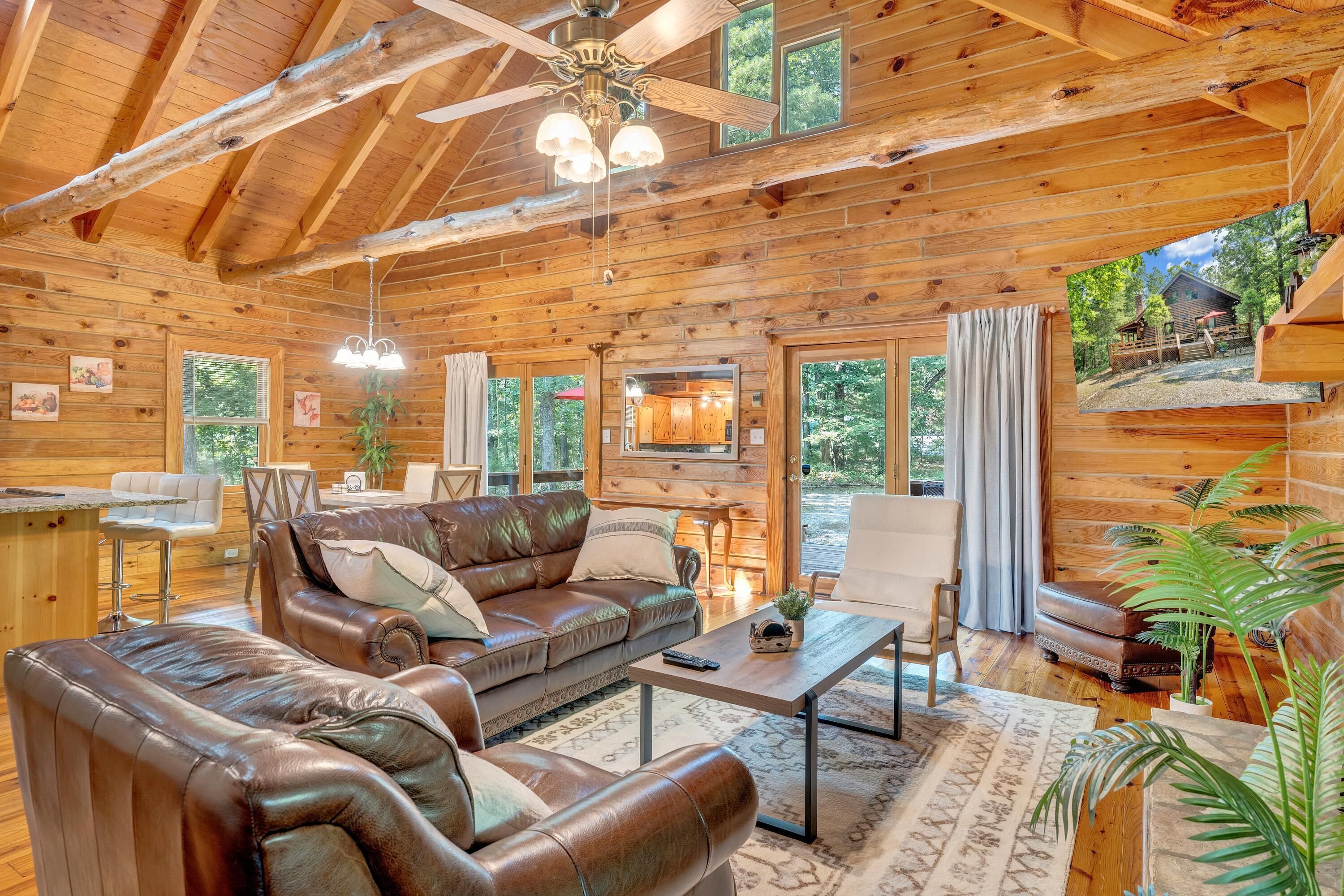 L’intérieur chaleureux d’un chalet en bois, avec un canapé en cuir, une table à manger et un coin cuisine visible à travers une fenêtre.