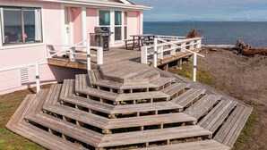 A pink building with a wooden deck leading to a balcony overlooking the sea. - Oceanfront House w/ Deck, Firepit & Mountain Views (Sequim)