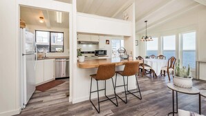 A modern kitchen with a bar area, wooden flooring, and a view of the sea. - Oceanfront House w/ Deck, Firepit & Mountain Views (Sequim)