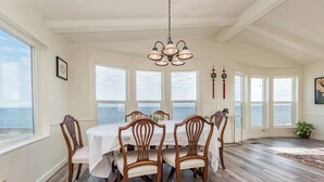 A dining room with a large table, six chairs, and a chandelier. There are large windows with a view of the ocean. - Oceanfront House w/ Deck, Firepit & Mountain Views (Sequim)
