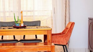 Een eetruimte met een houten tafel, twee grijze stoelen met kussens, en een rode fauteuil.