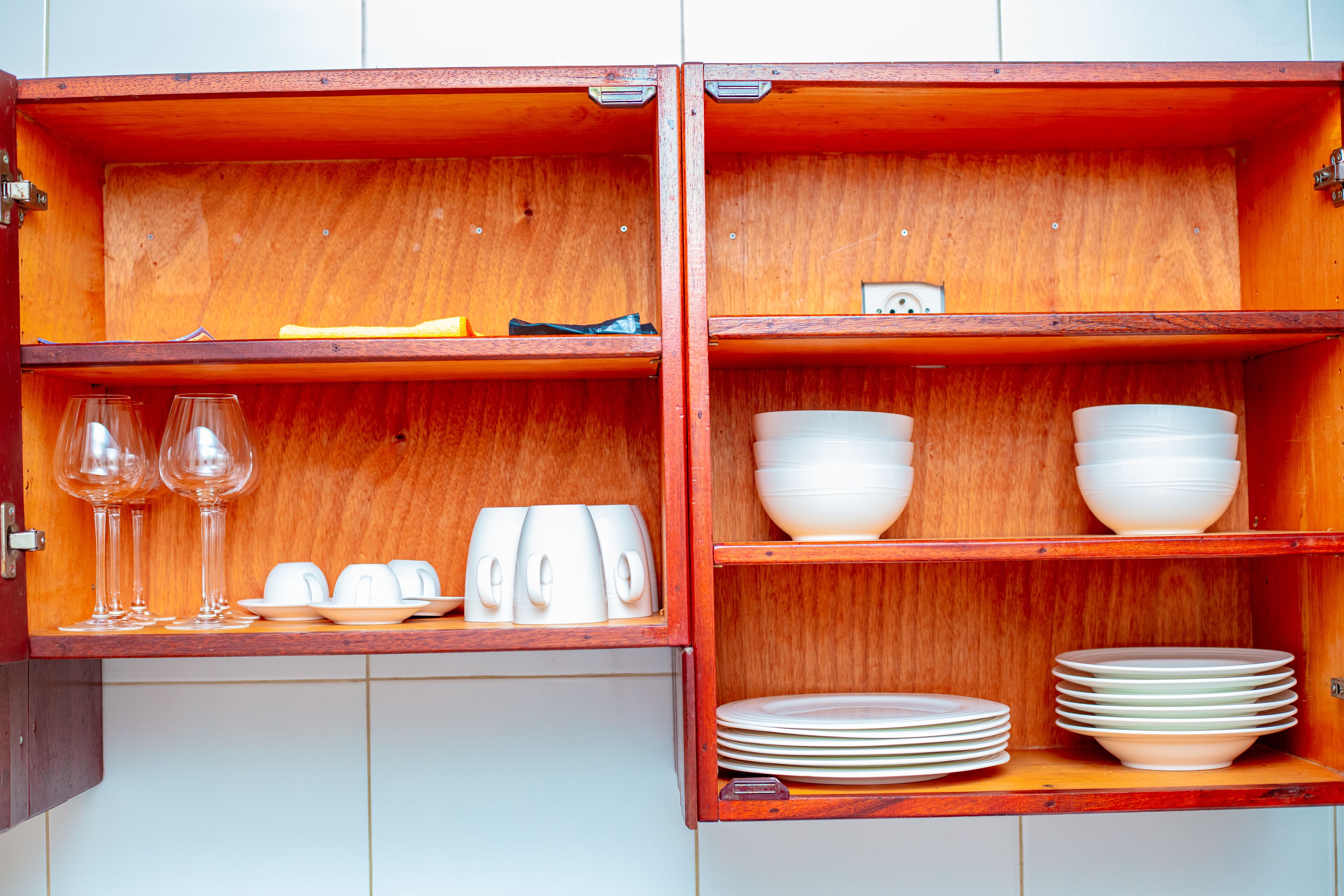 A wooden cabinet with shelves containing white cups, bowls, and plates.