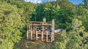 A cabin with multiple levels, large windows, and a stone exterior, surrounded by dense forest. - Mountain Dream’n- modern, dog friendly, hot tub (Blue Ridge)