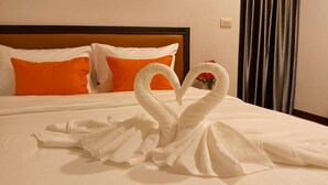 A hotel room with a neatly made bed, two orange pillows, and a heart-shaped towel arrangement on the bed. - THA PHAE VILLAGE (Chiang Mai)