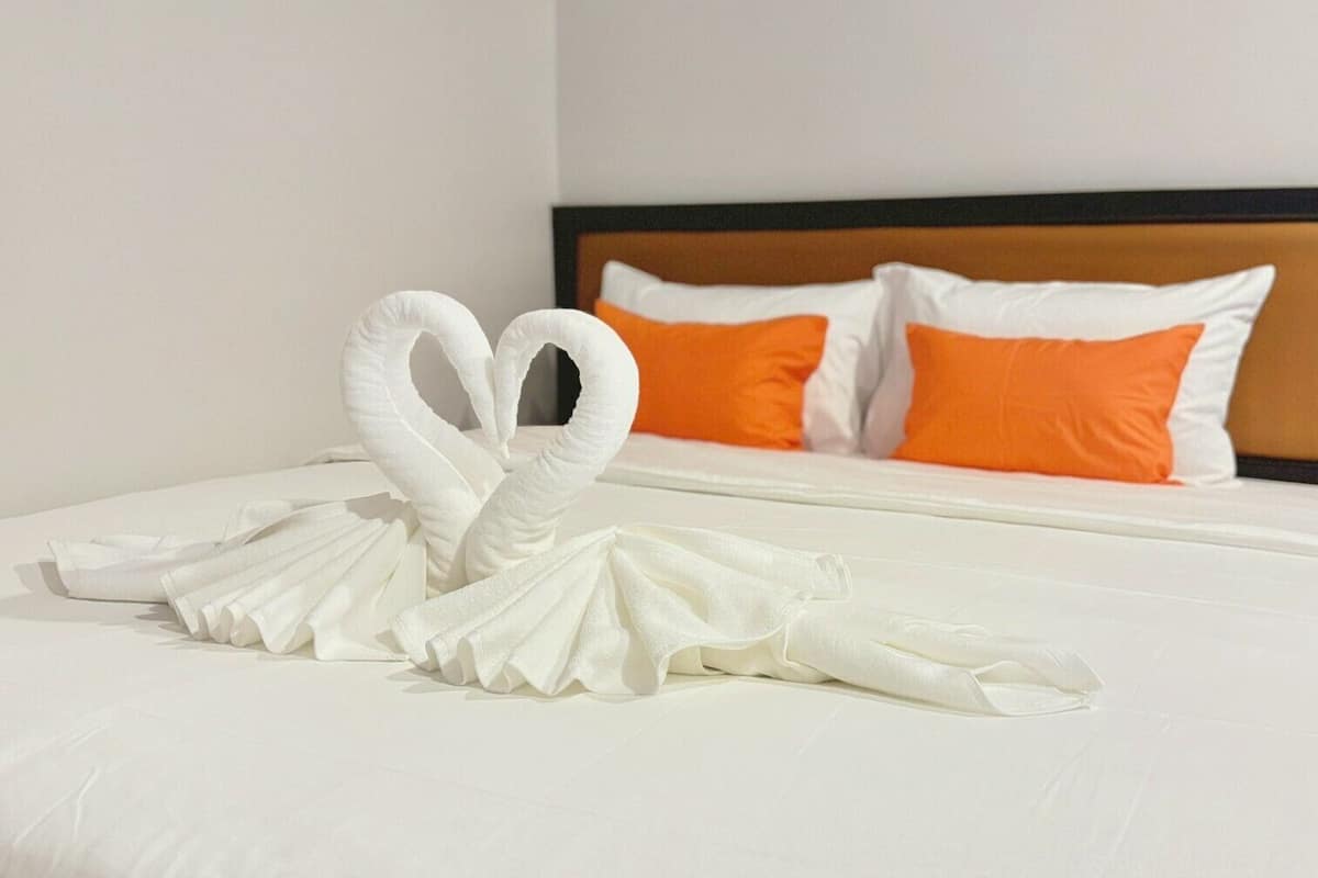 A neatly made bed with a swan towel art in a hotel room.