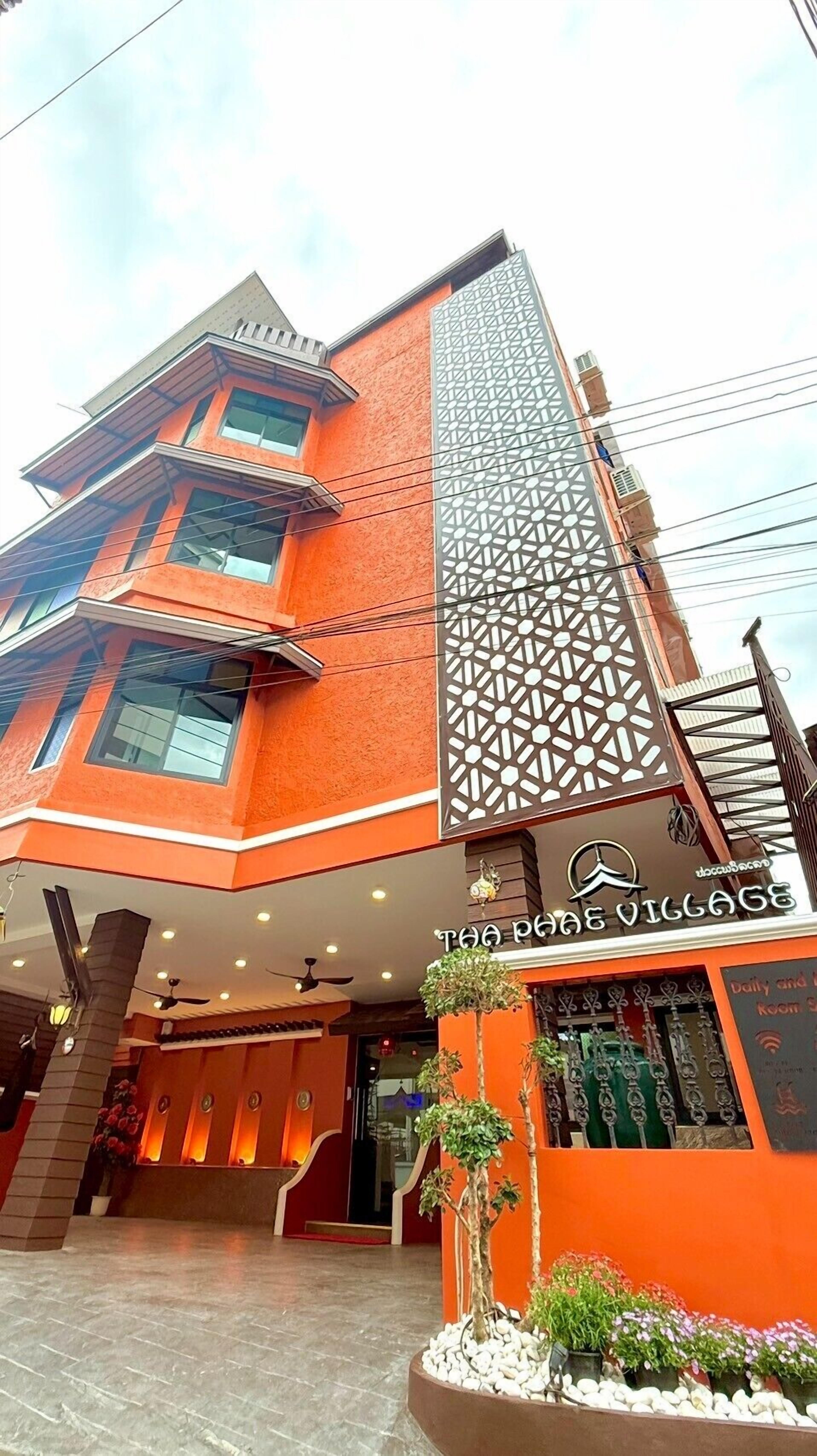 A multi-story building with a modern design, featuring a prominent vertical decorative panel and a sign reading "Tea House Village".
