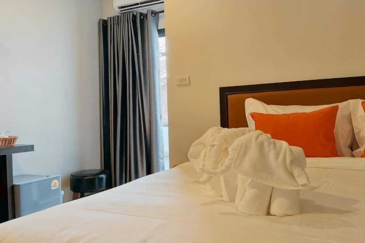 A hotel room with a bed, pillows, a small table, and a chair.