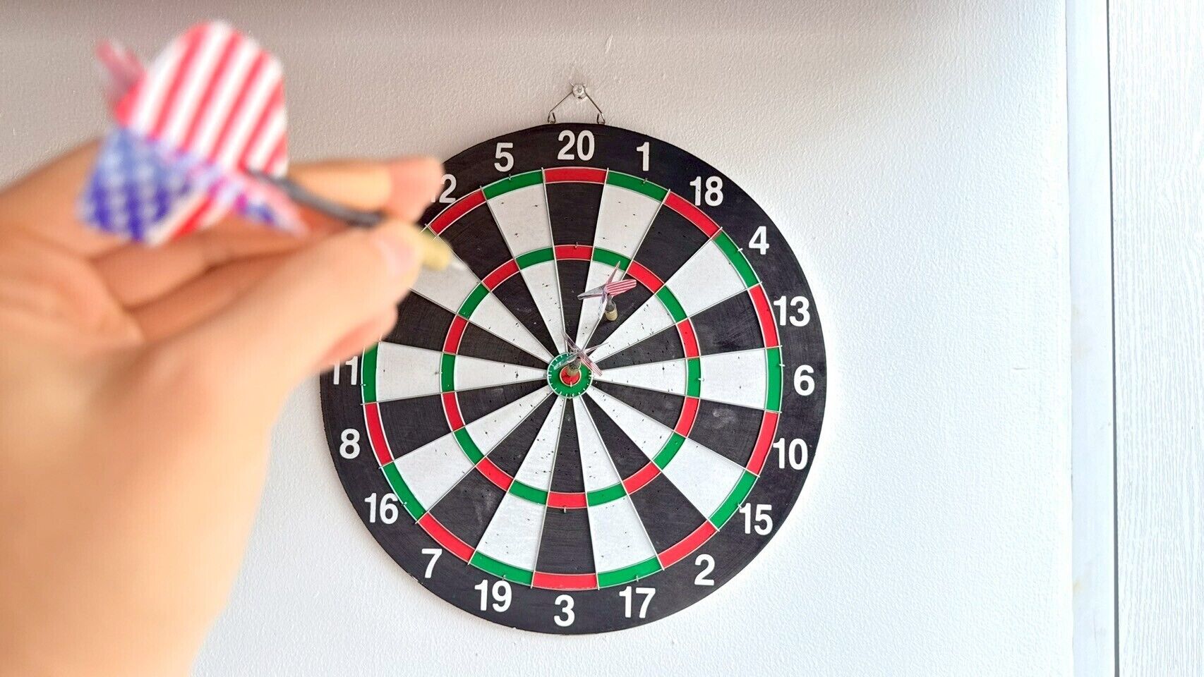 A hand holding a dart, aiming at a dartboard with numbers and colored segments.