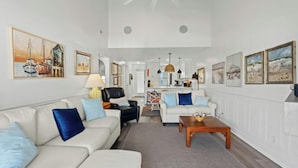 Een ruime woonkamer met een hoge plafond, een eethoek en een keuken op de achtergrond.