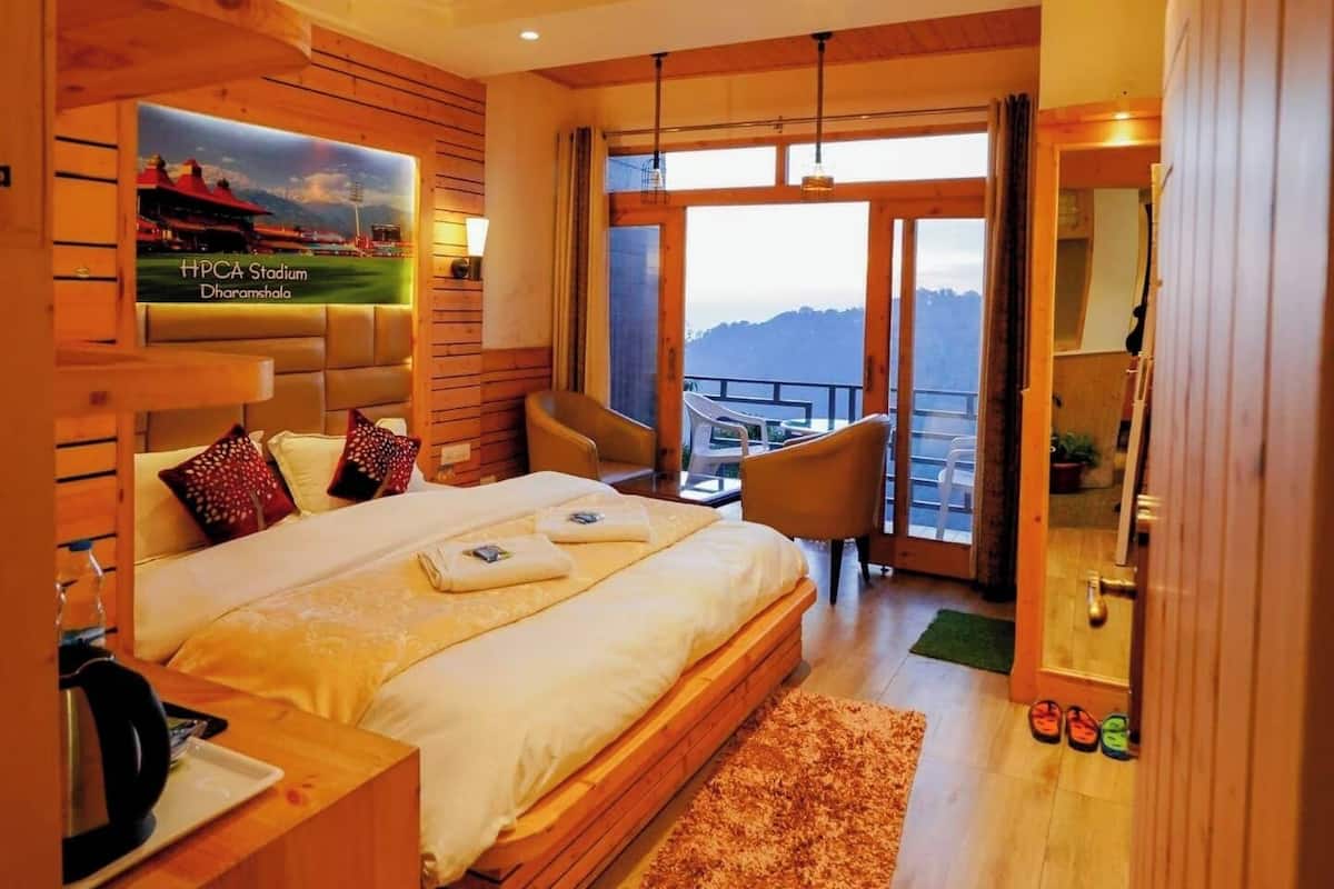 A hotel room with a large bed, a ceiling fan, a view of the mountains, and a balcony with chairs.