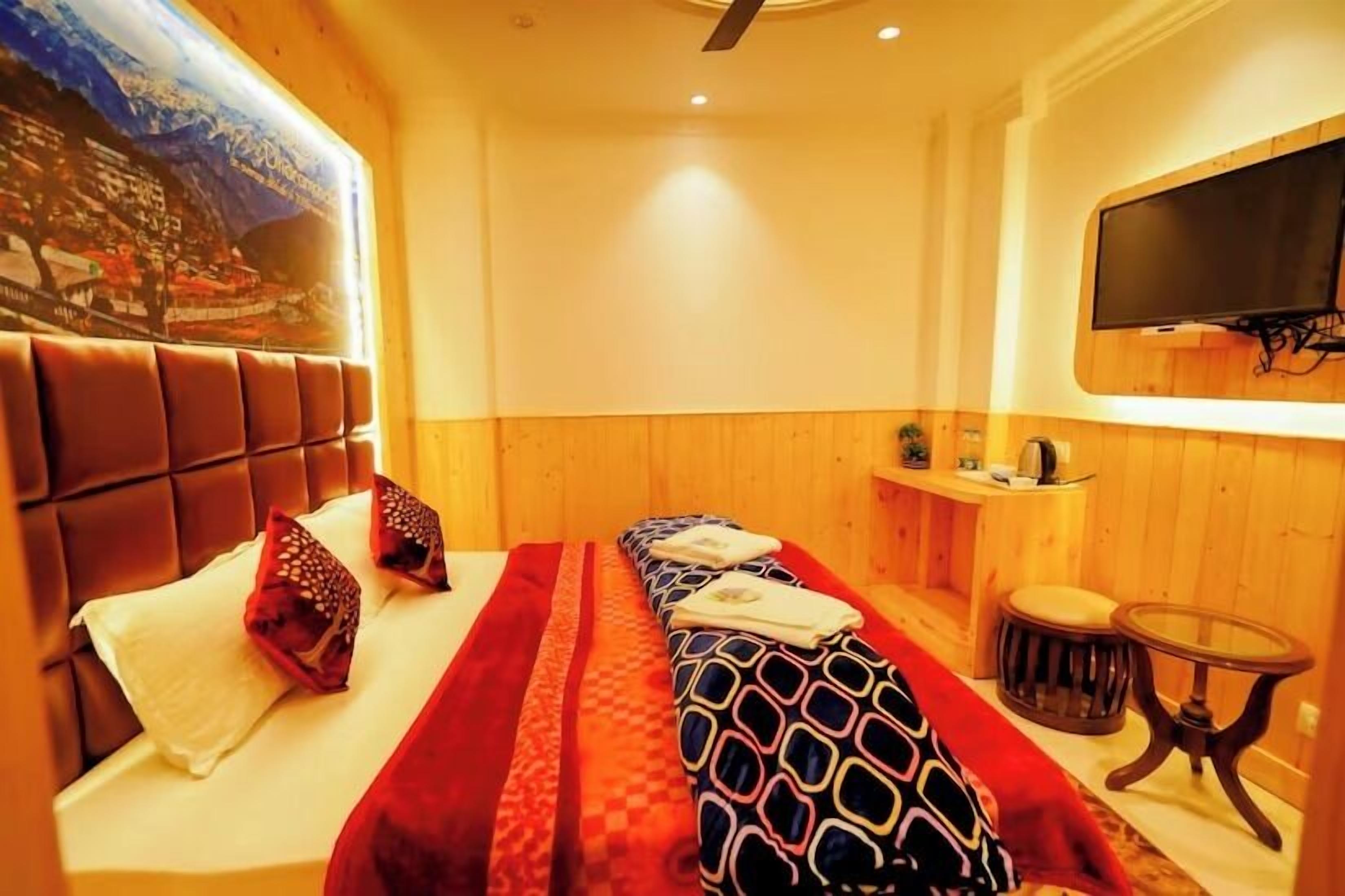 Quarto de hotel com cama, televisão na parede, mesa pequena e pintura na parede.