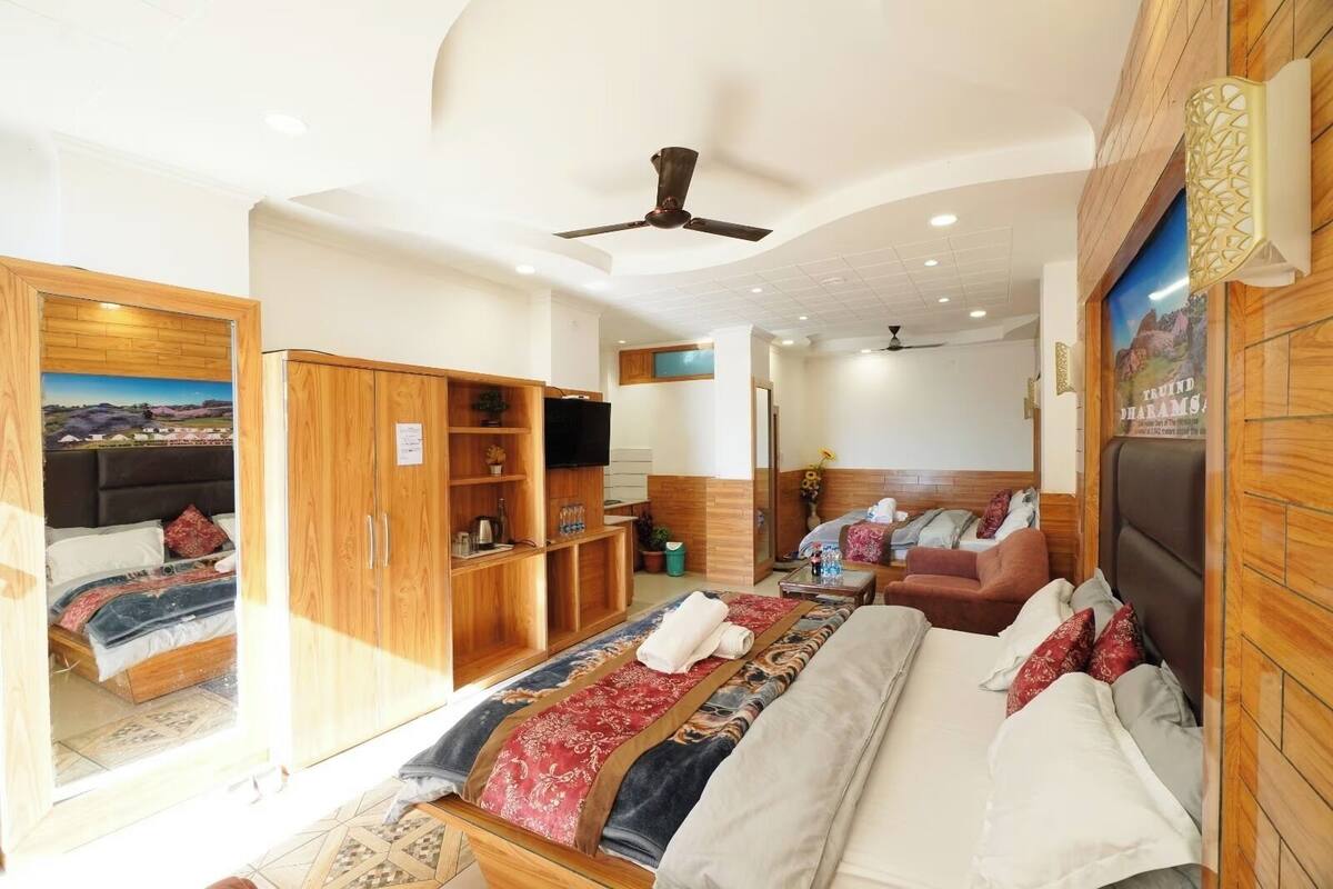 A spacious hotel room with a large bed, a wardrobe, a television, and a ceiling fan.