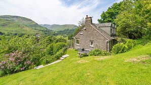 Une maison en pierre avec un toit en pente, une terrasse en bois et une vue sur des collines ondoyantes.