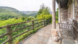 Un balcon dallé de pierres, avec une balustrade en bois, qui offre une vue sur une vallée verdoyante.