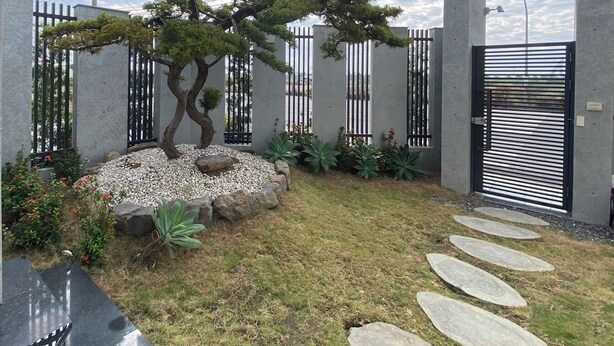 A modern garden with a bonsai tree, gravel path, and a metal gate. - Sky BnB (Donggang)