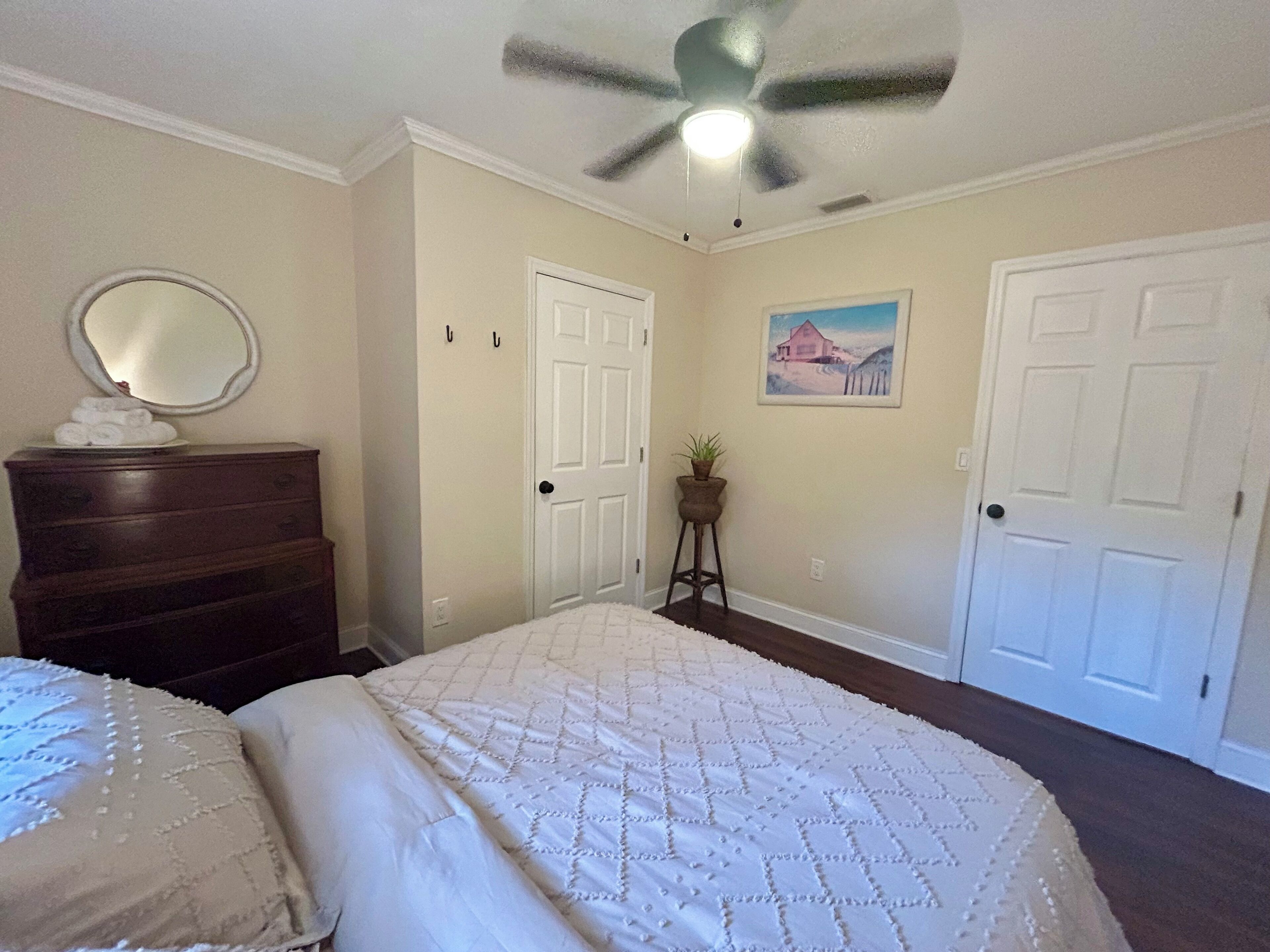 Een slaapkamer met een bed, een dressoir, een plafondventilator en een deur.