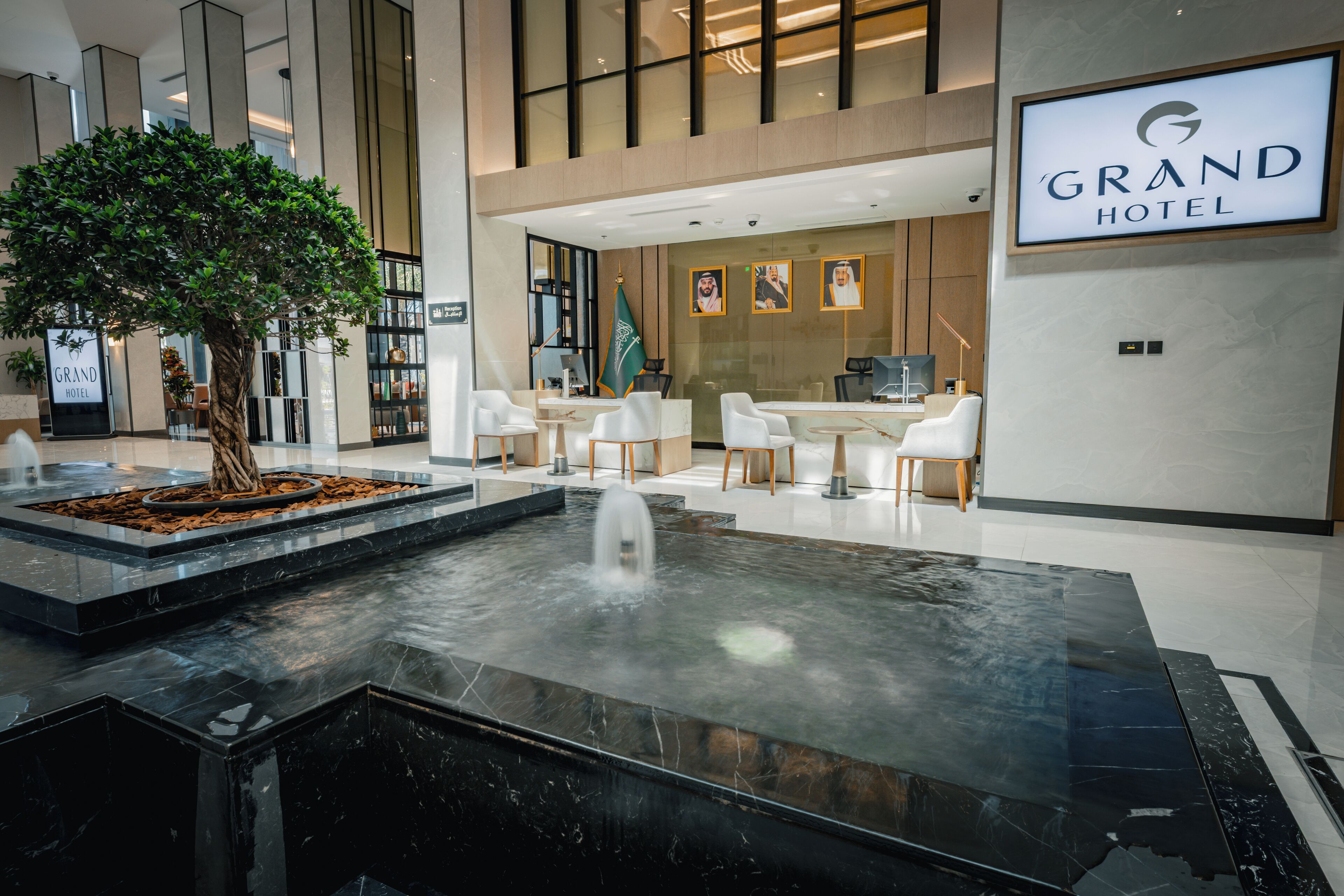 Un hall d’hôtel moderne agrémenté d’un élément décoratif aquatique, d’un espace salon et d’un comptoir d’accueil.