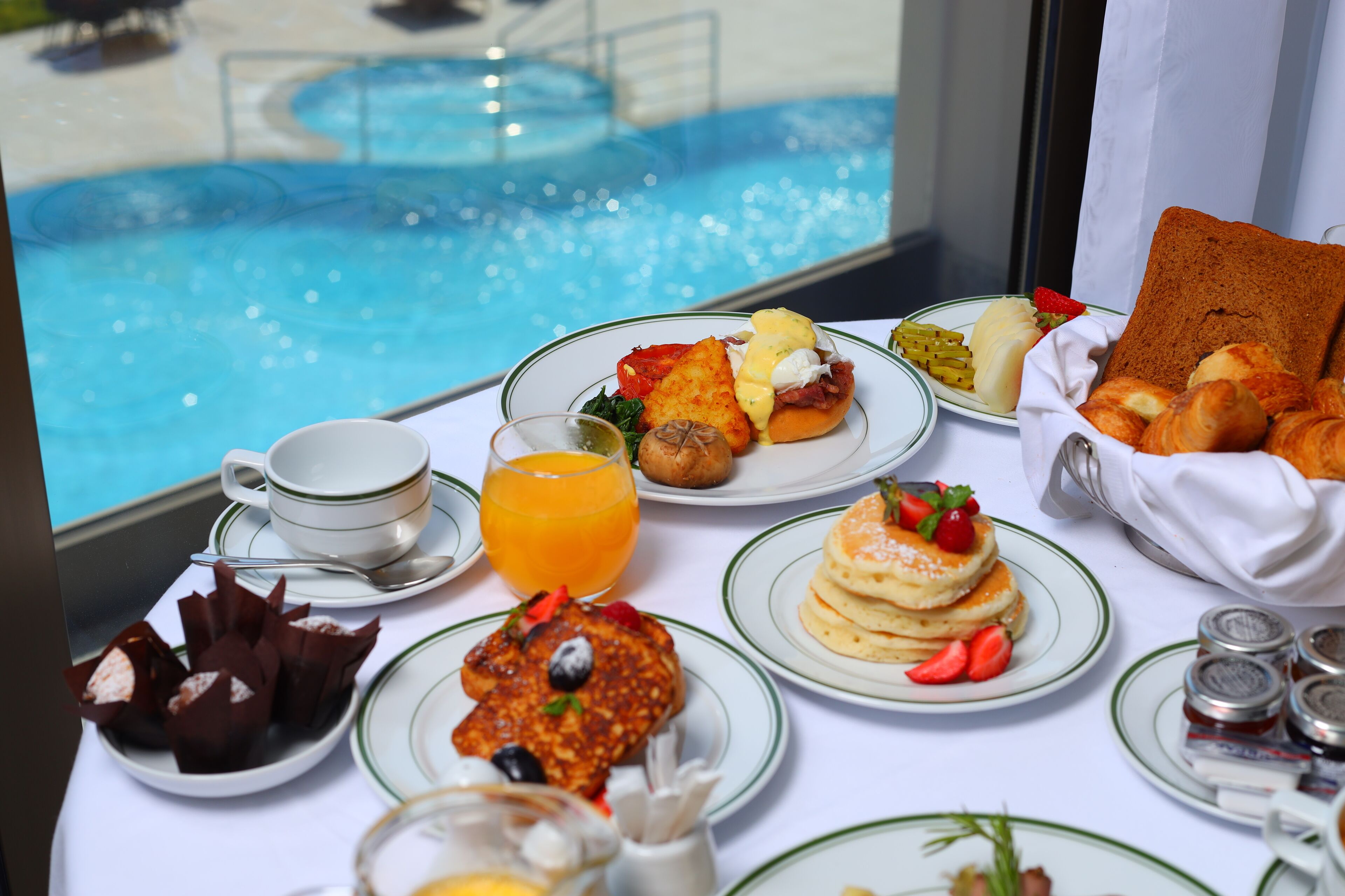 A breakfast buffet with various dishes, a pool view, and a window with curtains.