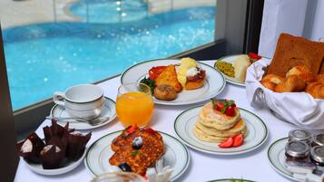 A breakfast buffet with various dishes, a pool view, and a window with curtains.