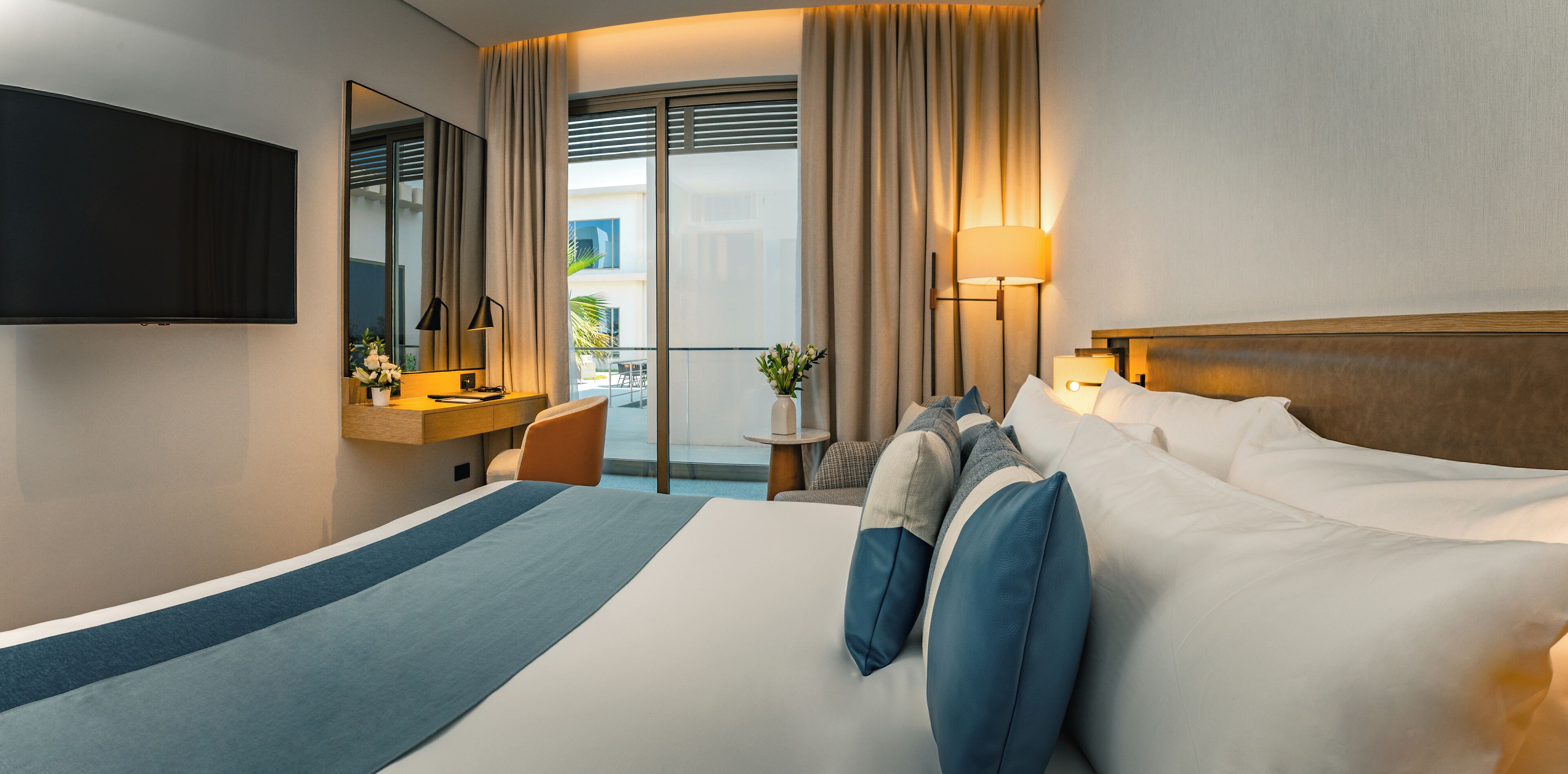Une chambre d’hôtel avec un grand lit, un bureau avec une chaise, un téléviseur fixé au mur et un balcon avec des rideaux.
