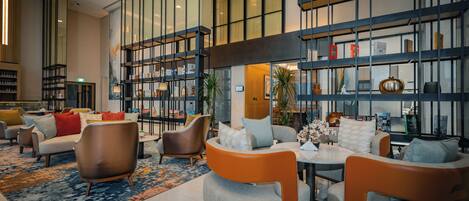 A modern hotel lobby with seating areas, a coffee table, and a bookshelf.