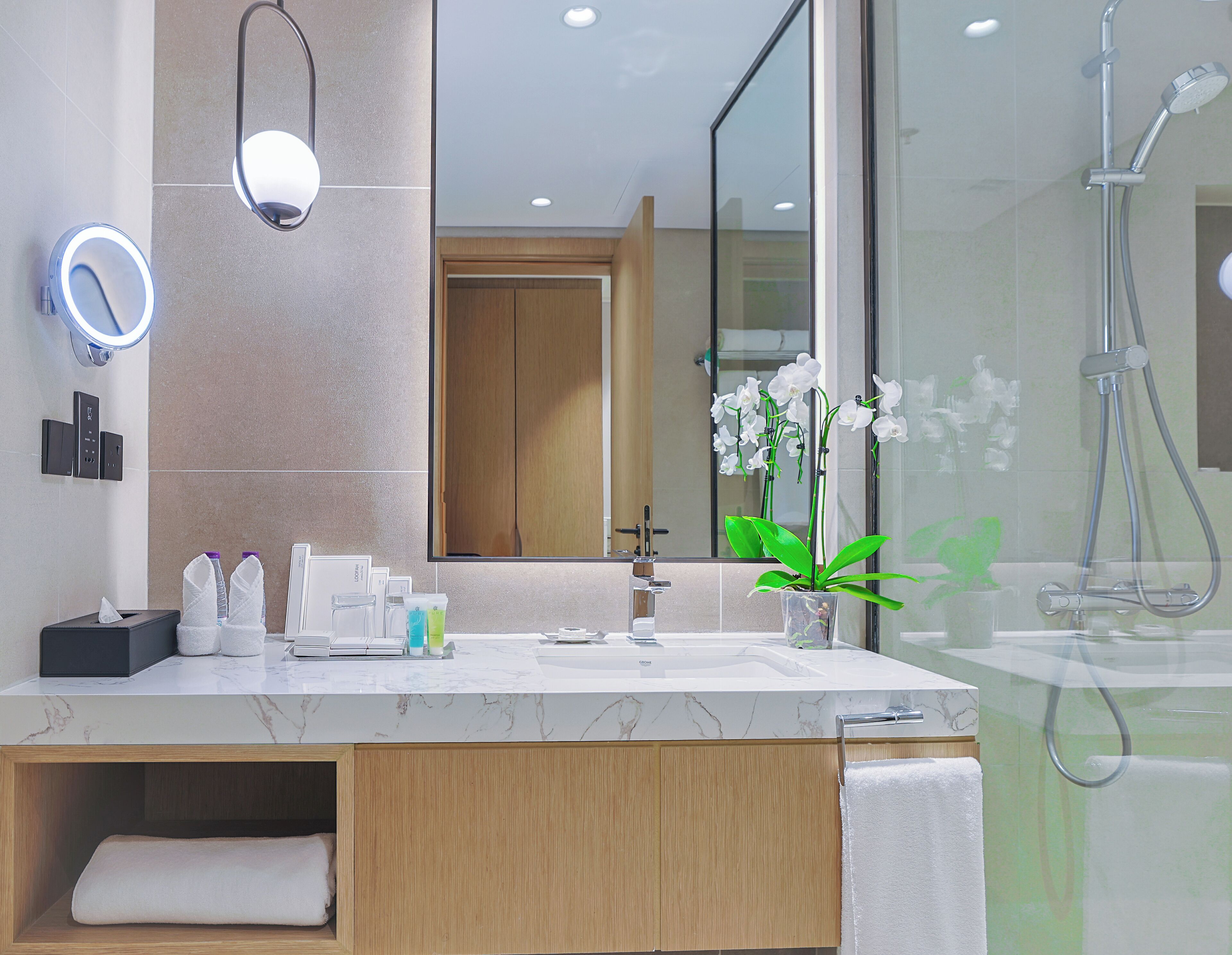 Une salle de bain moderne avec un meuble-lavabo en marbre, un grand miroir, une douchette à main et une orchidée en pot.
