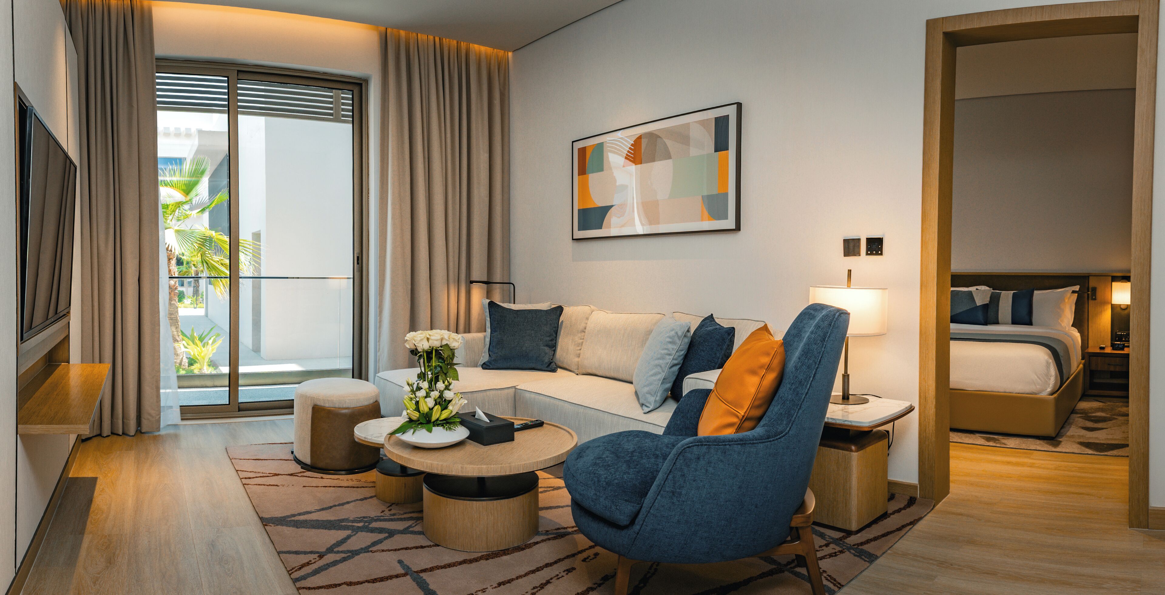 Una habitación de hotel moderna con sofá, sillón, una mesa de centro redonda y una cama.