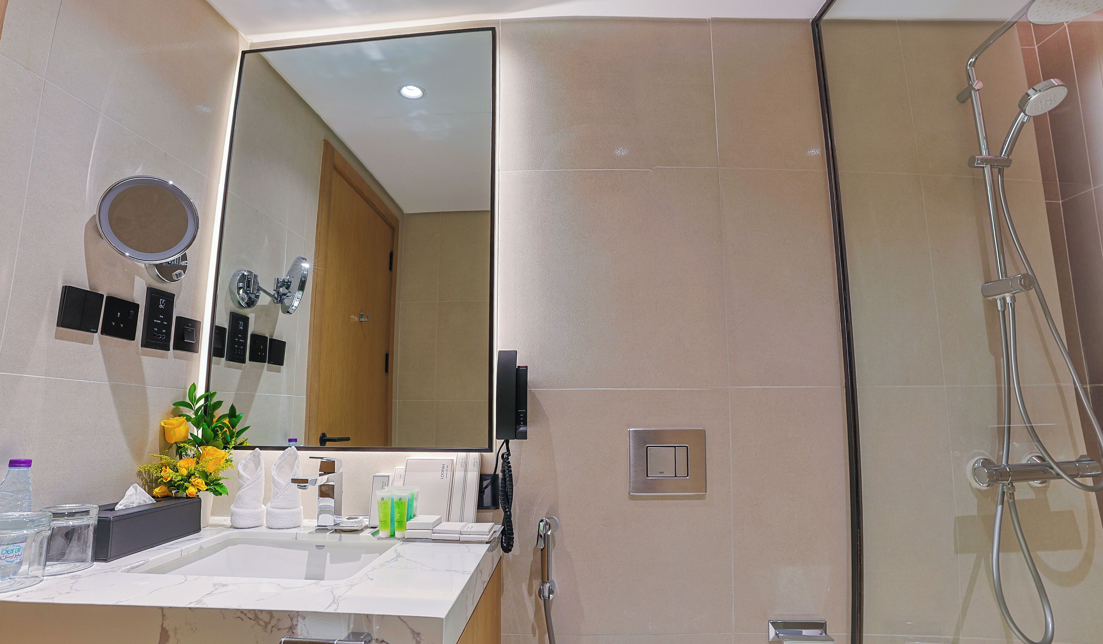 A modern bathroom with a large mirror, a shower, and a vanity with toiletries.