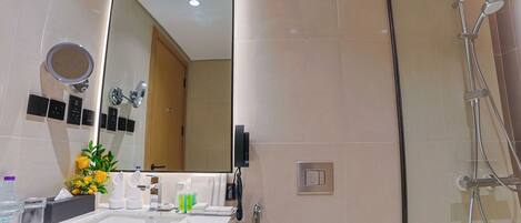 A modern bathroom with a large mirror, a shower, and a vanity with toiletries.