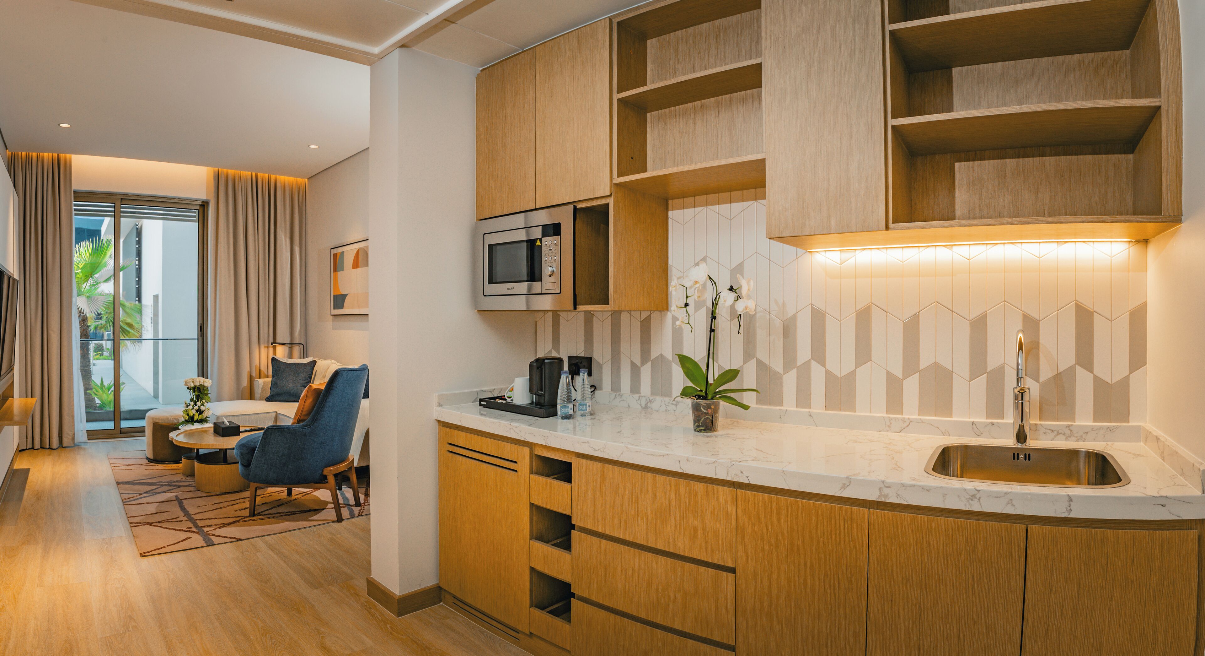 A modern kitchen with wooden cabinets, a built-in microwave, and a marble countertop.