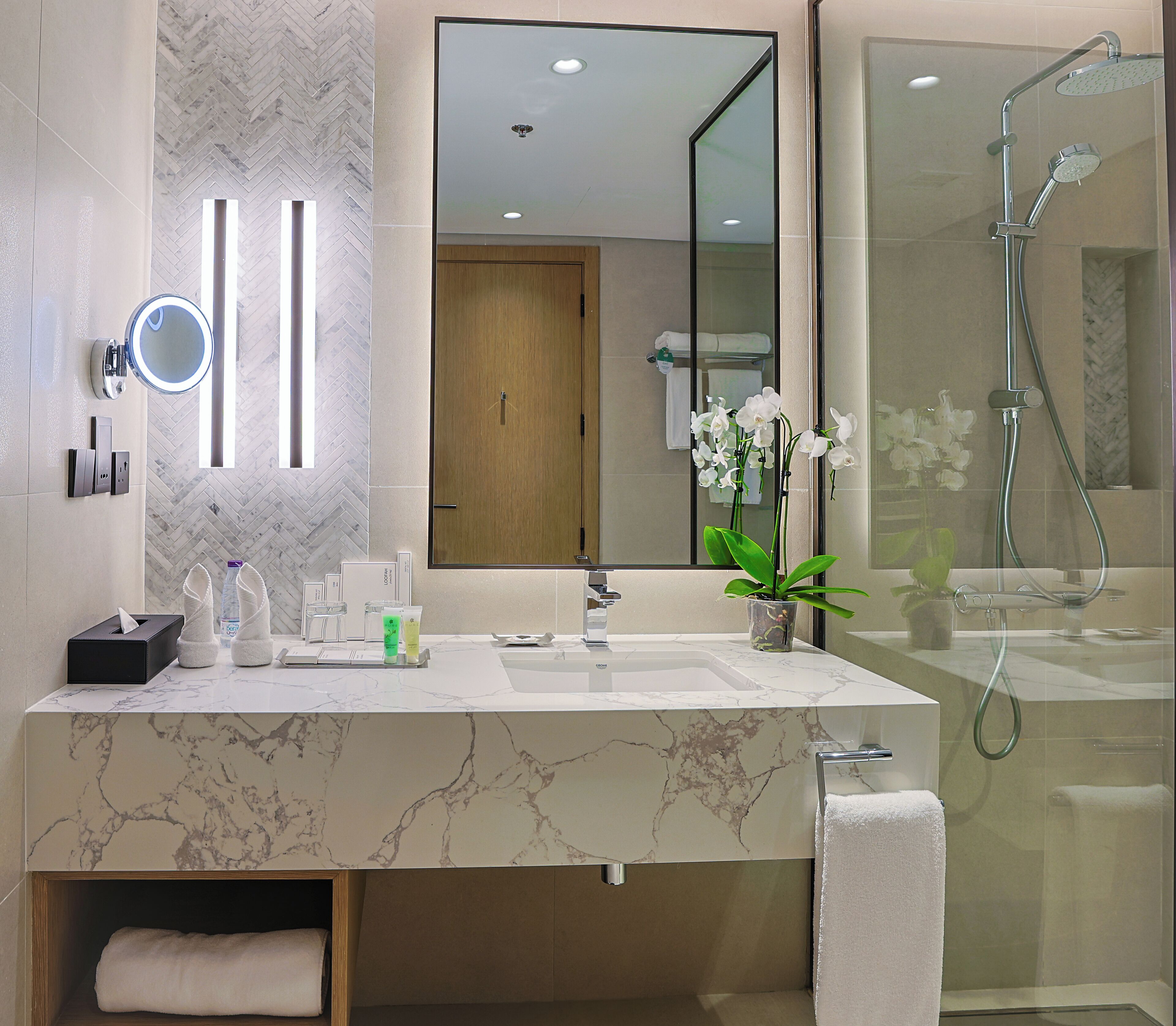 Un baño moderno con tocador de mármol, un espejo grande, un cabezal de ducha de mano y una orquídea en maceta.
