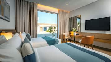 Habitación de hotel con dos camas, un escritorio, una silla, un televisor y un ventanal con cortinas.