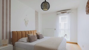 Une chambre à coucher avec un lit, des tables de chevet, un luminaire suspendu et une fenêtre avec des rideaux.