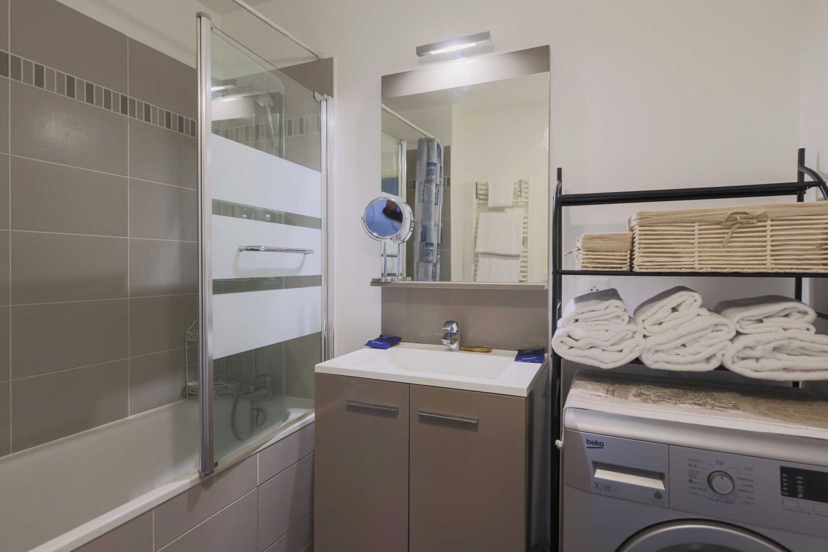 Une salle de bain avec une douche à parois de verre, un lavabo avec un miroir et un lave-linge.