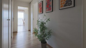 Un couloir doté d’un plancher en bois, d’une plante en pot et de trois œuvres d’art encadrées accrochées au mur.