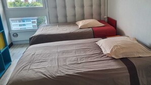 Ein Zimmer mit zwei Betten, jeweils mit Kissen und Kopfteil. Ein Fenster bietet Blick auf Gebäude.