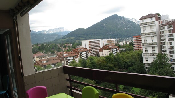 Ein Balkon mit Blick auf eine Wohngegend, darunter Wohnhäuser und Berge im Hintergrund.
