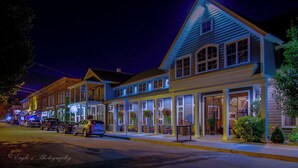 A row of brightly lit, multi-story buildings with large windows and outdoor seating areas, suggesting a commercial or mixed-use property. - Walk to Holiday Valley, Family-sized House, Sleeps 9, Shuffleboard, 2 fireplaces (Ellicottville)